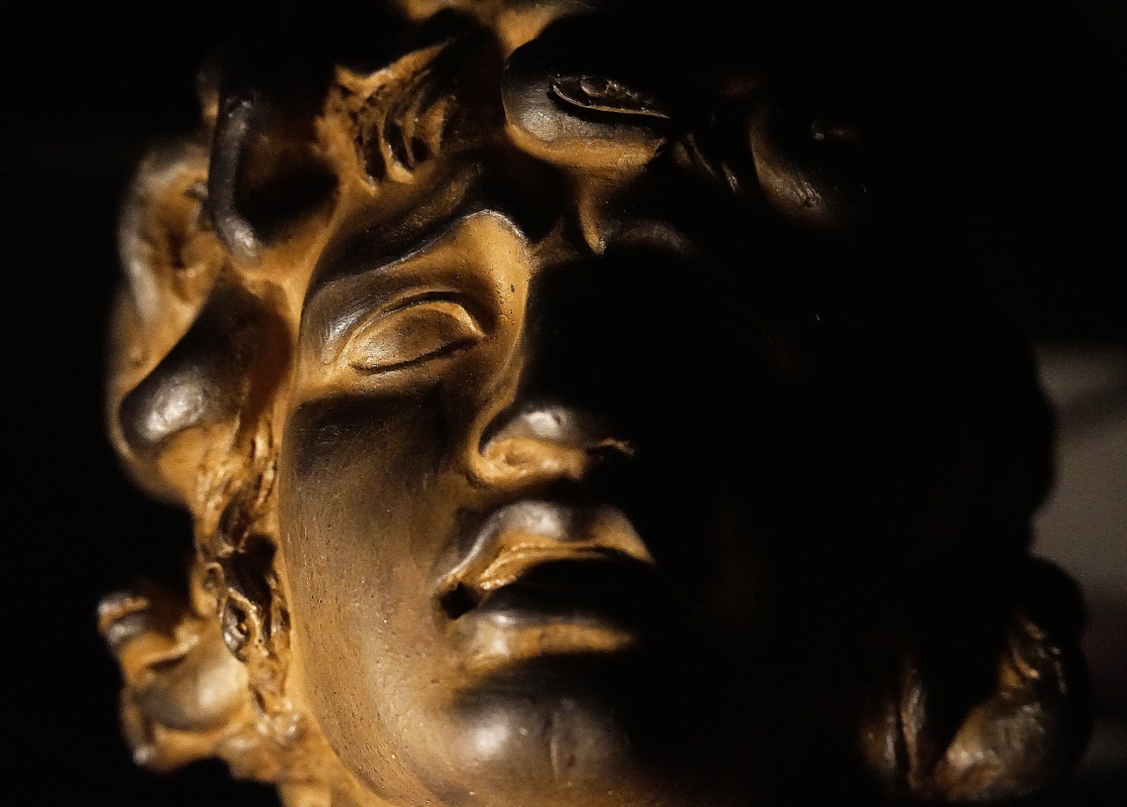 Rostro escultórico en primer plano con luz lateral y una mitad del rostro en sombra.